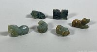 Six jade carved animal pendants arranged on a surface showing their size and relative shapes