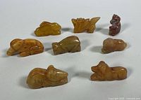 Eight hand carved animal pendants made from yellow jade displayed together showing their varied shapes and sizes, confirming quantity and condition.