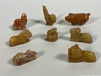 Eight hand-carved yellow jade animal pendants arranged together showing natural color variations and shapes