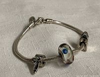 Full view of a 7-inch Pandora sterling silver snake chain charm bracelet with three attached charms including one glass bead and two silver shoe-shaped charms.