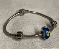 Side view of charm bracelet showing chain and charms including blue glass bead and silver charms