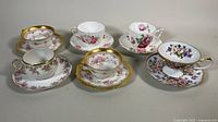 All six teacup and saucer sets arranged in two rows, showing variety in floral patterns and gold accents