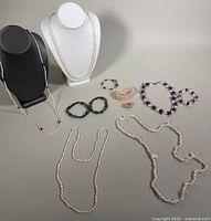 Entire assortment of pearl and button pearl jewelry displayed on black and white stands and laid on table.