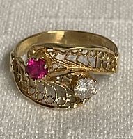 Front view of children's gold ring showing the ruby and crystal stones with filigree band.