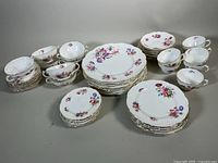 Full set showing stacks of dinner plates, luncheon plates, dessert plates, teacups and saucers, and cream soup bowls all decorated with floral designs and gold edging.