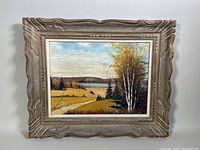 Framed oil painting showing a scenic autumn landscape with a dirt path, trees, a lake and hills.
