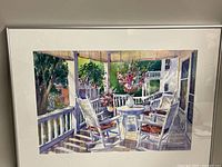 Framed watercolour painting depicting porch scene with two white rocking chairs, table with flower vase, porch railing and house background.