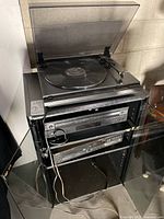 Overview of stereo stand with JVC AL-A151 turntable on top and two CD players below, showing glass magnetic doors and shelf wear.