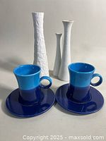 Front view of two-tone blue Rosenthal mugs and matching saucers with three white textured candleholders in background