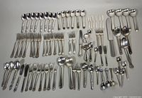 Wide view of the complete lot showing numerous spoons, forks, knives, and ladles laid out on a flat surface, various patterns visible.