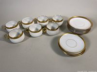 Six white porcelain teacups and twelve saucers arranged on table, showing overall lot