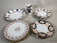 Several bone china plates and a small creamer pitcher arranged on a table, showing variety of patterns and styles in the lot.