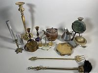 Wide shot of vintage metalware lot showing brass and copper items including kettles, candleholders, balance scale, and other brass decorative objects on white background.