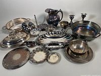 Photo showing collection of various vintage silver plated serving items including trays, bowls, gravy boat, pitcher, covered dish, and candleholders.