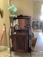Full view of antique cabinet showing overall shape, shelves, and green glass lamp on top.