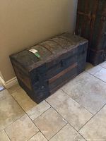 Full side view of humpbacked steamer trunk with wood slats, metal and tin panels showing wear and patina.