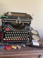 Front view of black Underwood Standard manual typewriter with round keys, accompanied by wooden frame clock with thermometer.