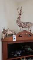 Pair of birch bark reindeer figurines with twig and berry antlers shown on top of wooden furniture.