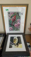 Two framed prints, one featuring a cardinal bird with pink blossoms, and another featuring a dog. Both are matted and framed.