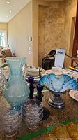 Opalescent blue brides basket, blue candleholders, and clear glass compote dishes arranged on countertop.