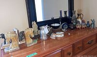 Full view of wooden dresser top with marble horsehead bookends, elephant figurine, silver pitcher, trinket boxes, geode, multiple vases, Mexican animal figurines, chime, and other decorative items.