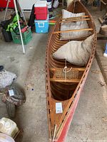 Bow-down angled view showing internal cedar strip ribs, webbed seat rack, and patterned cushions within red canvas hull