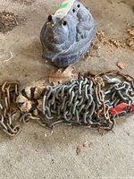 Photo showing the cast iron roaster pot lid with relief design resembling an animal face and bundled metal chains on the floor.