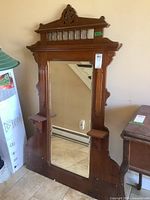 Front angled view of large vertical dresser mirror showing ornate Eastlake wood frame and small shelves on each side