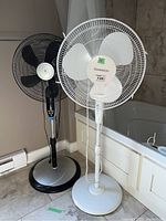 Two standing fans side by side; one black Weatherworks fan and one white Garrison fan.