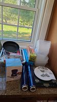 Wide view of lot on kitchen counter showing food storage containers, plastic wrap rolls, aluminum trays, frying pan, kitchen scale, and boxed fondue set.