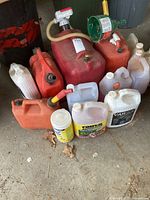 Wide view showing multiple gas and fluid containers of various sizes and colors including a large red container with a pump and other containers labeled Varsol and windshield washer fluid.