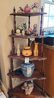 Full view of wooden corner shelf with five levels holding various decorative items including birds, flowers, glass apple, wooden and ceramic containers, and barnacles figurine.