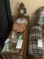 View of the entire set showing the clock, cheese and cracker board, and ink well set placed on wooden surface next to a plaid upholstered chair.