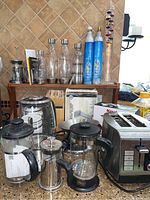 Photo showing the entire lot on a kitchen counter, including the toaster, four French presses, glass bottles with pour spouts, SodaStream cylinders, and Galileo thermometer, as well as boxes of KitchenAid accessories.