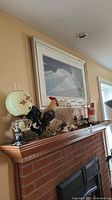 Wide view of the mantel showing wood boomerangs, glass lamps, resin rooster, coral and seashell arrangement, and painted vase