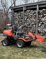 Side view of Husqvarna R1751 lawn tractor parked outdoors against stacked firewood.