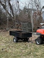 Front and side view of black metal framed lawn tractor trailer attached to orange tractor