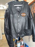 Front view of black genuine leather vest featuring snap button closure and Harley Davidson patch on chest
