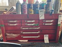 Front view of the red metal toolbox organizer showing three drawers with silver handles, labeled with tags, with various spray cans and items on top.