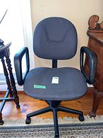 Front view of the grey fabric office chair showing the padded seat, backrest, black armrests, and five-wheel base on wooden floor.