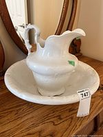 Overall view of white ceramic pitcher sitting inside matching basin on wooden surface