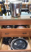 Kitchen drawers open, containing various pans including cast iron skillet and another large pan with lid, and the stock pot on counter above.