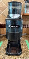 Front view of the Rancilio coffee grinder showing hopper filled with coffee beans and logo on front.