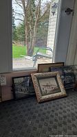 Photo showing various framed and laminated prints leaning against a window, sizes vary with one ornate frame visible.