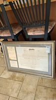 Full view of framed letters patent leaning against chairs on tile floor