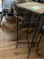 View of ceramic jug next to the small plant table, showing details of the glaze and handle on jug and metal frame legs of table.