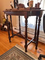 Side angle view of wooden side table showing turned legs, cross braces, and surface marks.