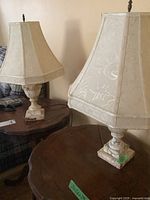 Two matching table lamps placed on wooden tables beside a sofa, showing fabric lampshades and marble bases.