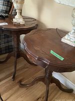 Pair of matching solid wood round tables with carved decorative tops and tripod legs shown side by side.