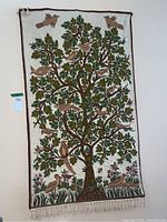 Full view of tree and birds tapestry hanging on a wall with visible fringe and tag.